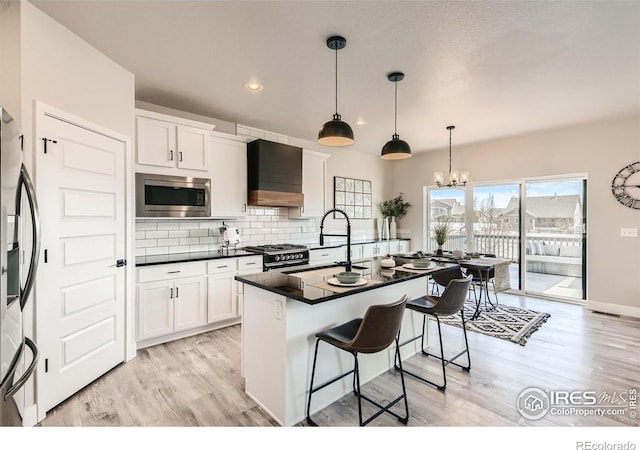 kitchen featuring premium range hood, stainless steel appliances, sink, white cabinetry, and hanging light fixtures