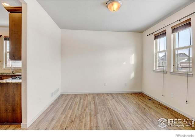 empty room with light wood-type flooring, visible vents, and baseboards