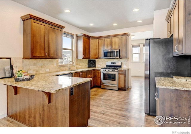 kitchen with light stone counters, a peninsula, a sink, appliances with stainless steel finishes, and brown cabinets