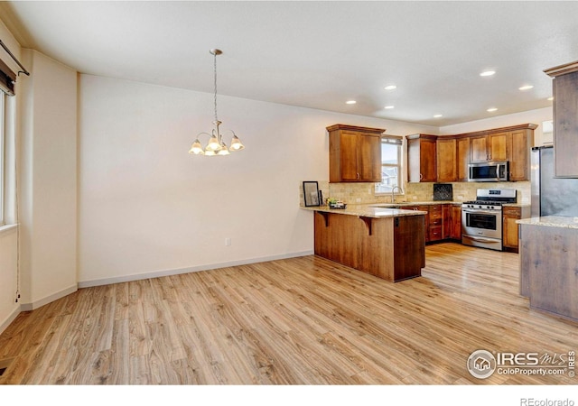 kitchen with a peninsula, appliances with stainless steel finishes, brown cabinetry, a kitchen bar, and pendant lighting