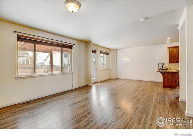 unfurnished living room featuring a textured ceiling, visible vents, baseboards, light wood finished floors, and an inviting chandelier