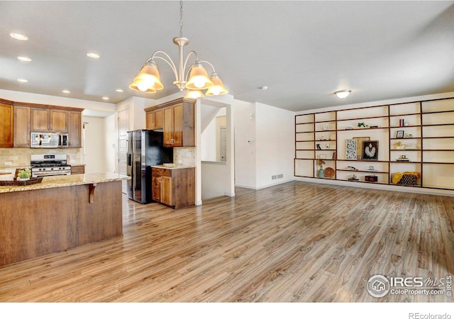 kitchen with stainless steel appliances, brown cabinetry, hanging light fixtures, and a kitchen bar