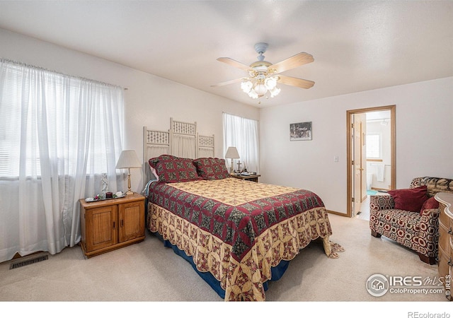 bedroom with ceiling fan, light colored carpet, and ensuite bath