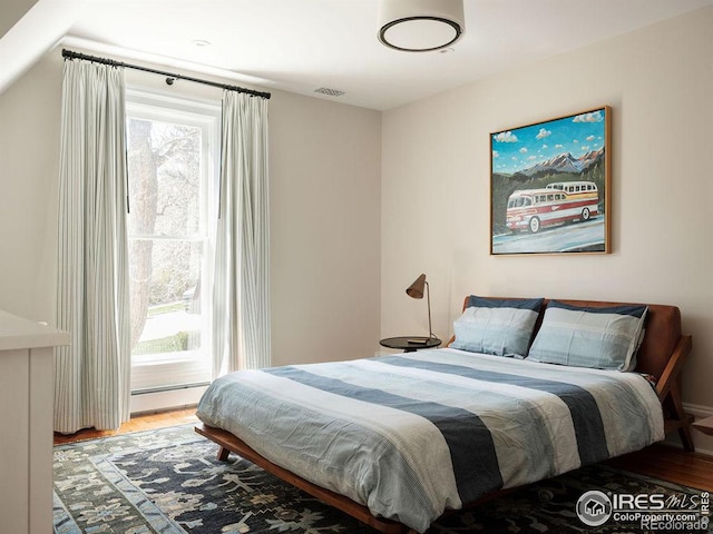 bedroom with wood-type flooring, multiple windows, and a baseboard heating unit