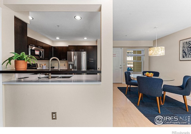 kitchen featuring light hardwood / wood-style flooring, hanging light fixtures, appliances with stainless steel finishes, sink, and dark brown cabinetry