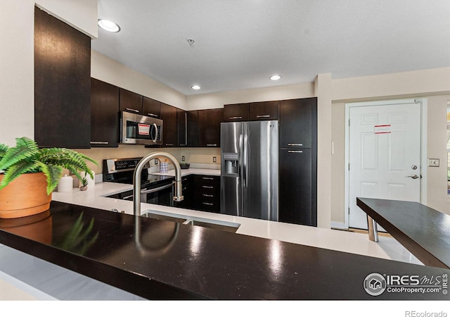 kitchen featuring sink, kitchen peninsula, appliances with stainless steel finishes, and dark brown cabinets