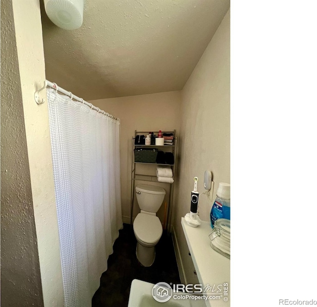 bathroom with a shower with curtain, a textured ceiling, and toilet