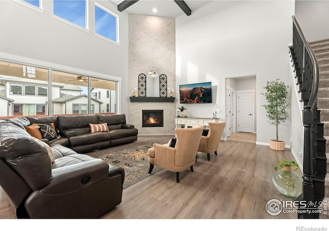 living room with a towering ceiling, a fireplace, light wood-type flooring, and beamed ceiling