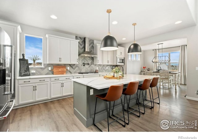 kitchen with a center island with sink, appliances with stainless steel finishes, wall chimney range hood, and white cabinetry