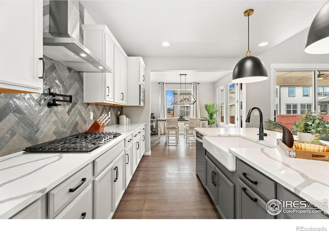 kitchen with appliances with stainless steel finishes, wall chimney exhaust hood, hanging light fixtures, and white cabinetry