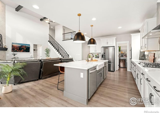 kitchen with wall chimney exhaust hood, pendant lighting, a center island with sink, white cabinets, and appliances with stainless steel finishes