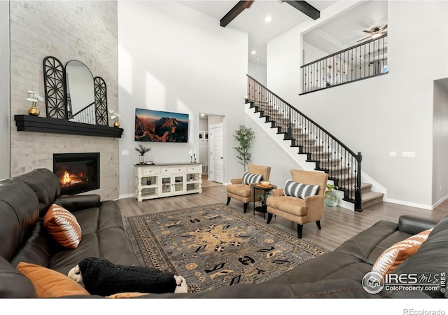 living room with a high ceiling, a large fireplace, ceiling fan, and wood-type flooring