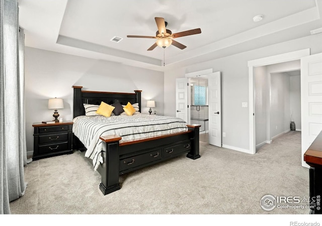 bedroom featuring ensuite bathroom, light carpet, ceiling fan, and a tray ceiling