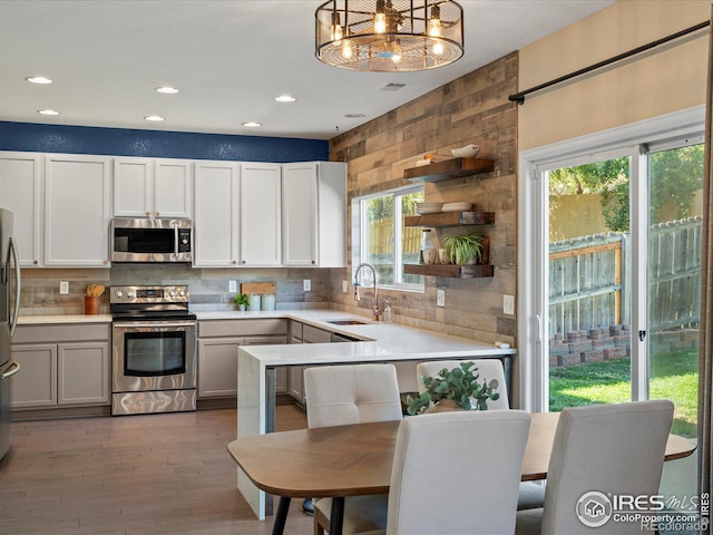 kitchen with appliances with stainless steel finishes, hanging light fixtures, a kitchen bar, sink, and white cabinetry