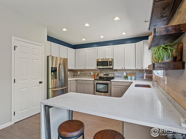 kitchen with a kitchen breakfast bar, stainless steel appliances, light wood-type flooring, kitchen peninsula, and sink