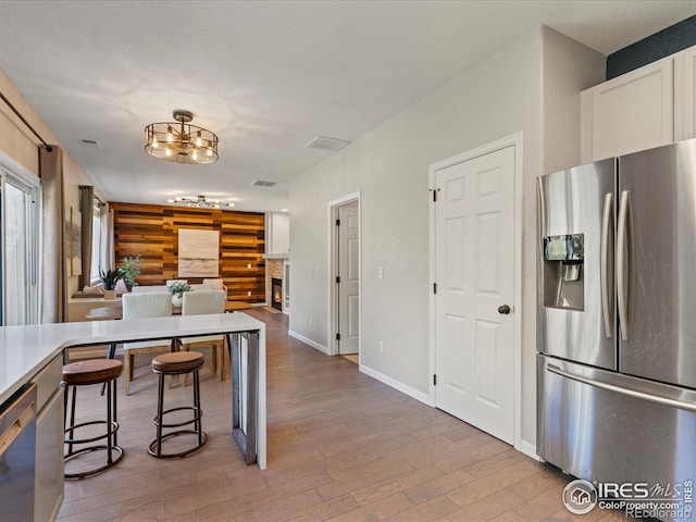 kitchen featuring hardwood / wood-style flooring, wood walls, a breakfast bar, a notable chandelier, and appliances with stainless steel finishes