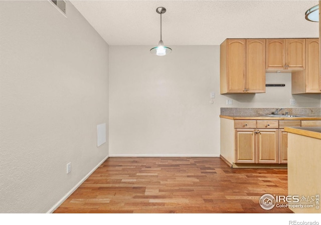 kitchen featuring light hardwood / wood-style floors, sink, light brown cabinetry, and decorative light fixtures