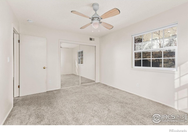 unfurnished bedroom featuring ceiling fan, light colored carpet, a closet, and a textured ceiling