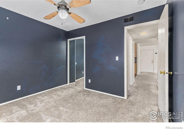 unfurnished bedroom with a textured ceiling, light colored carpet, a closet, and ceiling fan