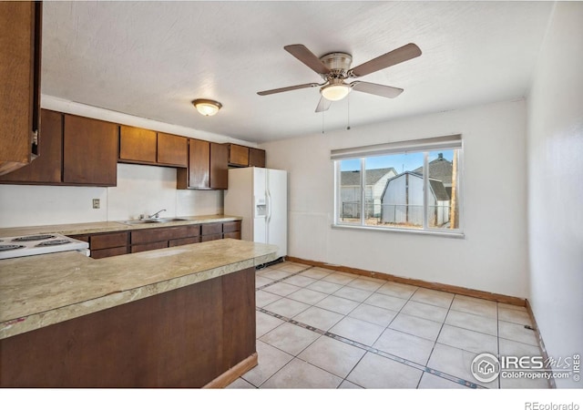 kitchen featuring white refrigerator with ice dispenser, range, light tile patterned floors, ceiling fan, and sink