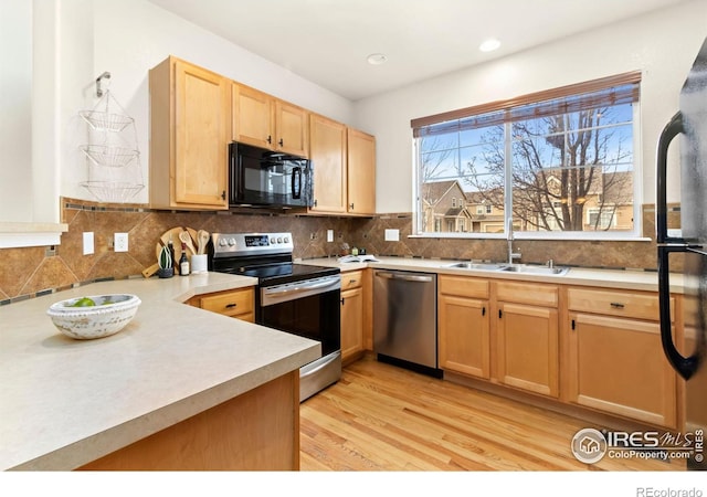 kitchen with black appliances, light hardwood / wood-style flooring, backsplash, and sink