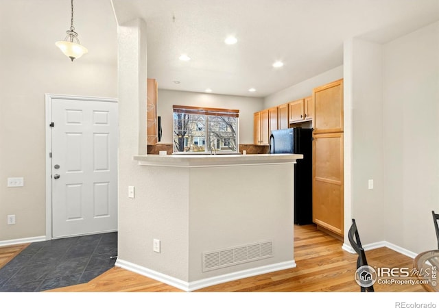 kitchen featuring decorative light fixtures, black fridge, hardwood / wood-style flooring, kitchen peninsula, and light brown cabinetry