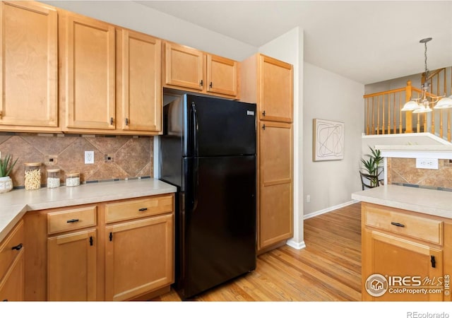 kitchen featuring black refrigerator, light wood-type flooring, backsplash, hanging light fixtures, and a notable chandelier