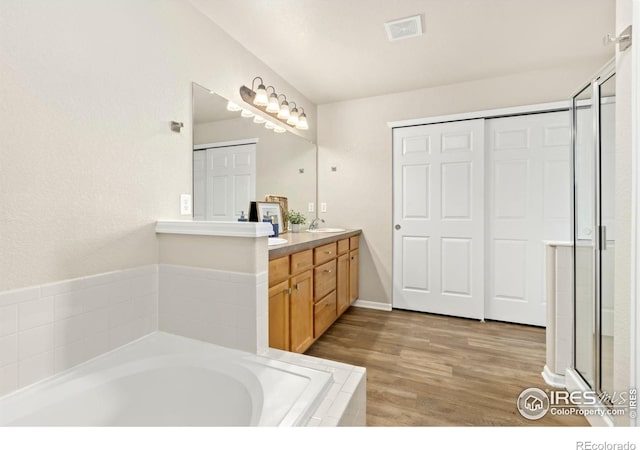 bathroom with hardwood / wood-style floors, tiled bath, and vanity