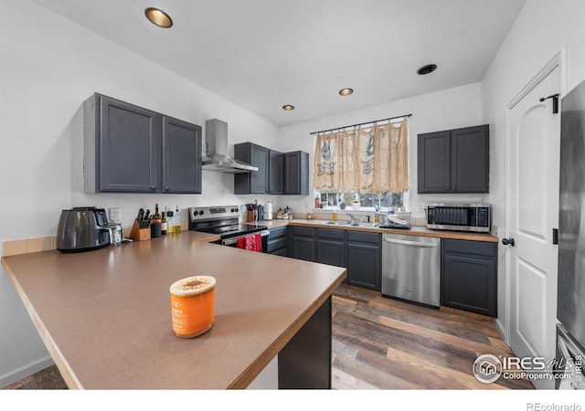 kitchen featuring kitchen peninsula, dark hardwood / wood-style floors, stainless steel appliances, wall chimney range hood, and sink