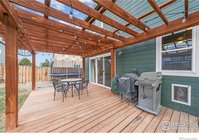 wooden terrace with grilling area, a pergola, and a trampoline