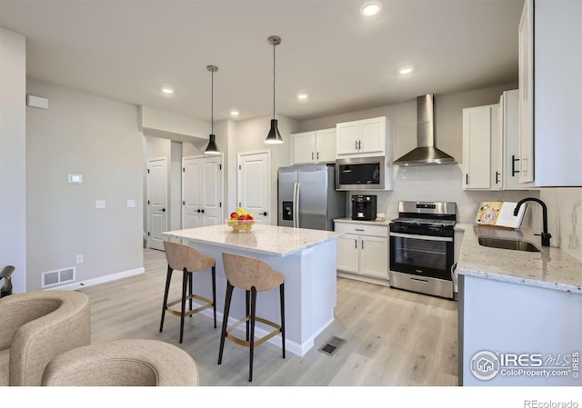 kitchen with appliances with stainless steel finishes, tasteful backsplash, wall chimney exhaust hood, white cabinets, and sink