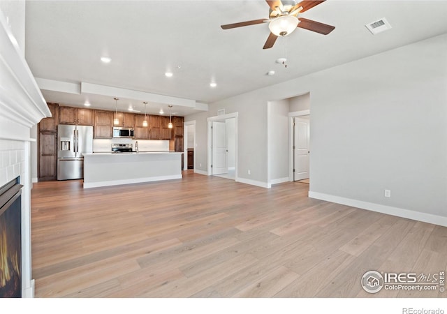 unfurnished living room with a tiled fireplace, ceiling fan, and light wood-type flooring