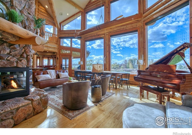 living room with high vaulted ceiling, light wood-type flooring, and a stone fireplace