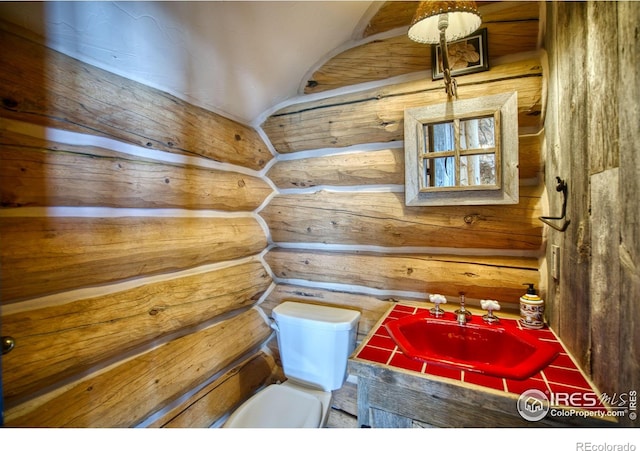 bathroom featuring toilet, rustic walls, and sink