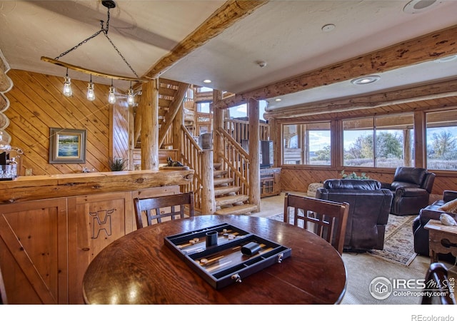 dining room with beam ceiling, light colored carpet, and wood walls