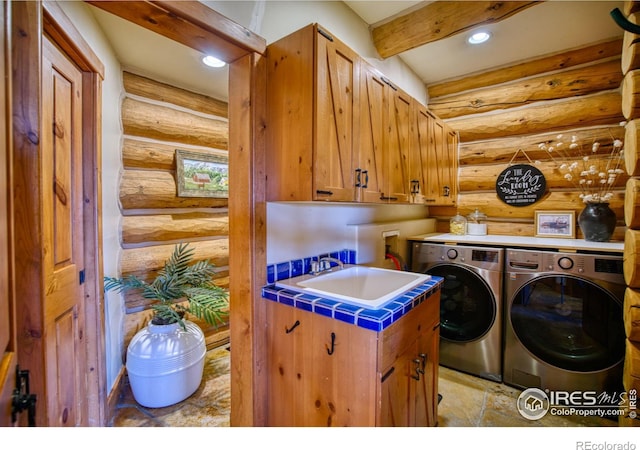 laundry room with log walls, cabinets, washing machine and clothes dryer, and sink