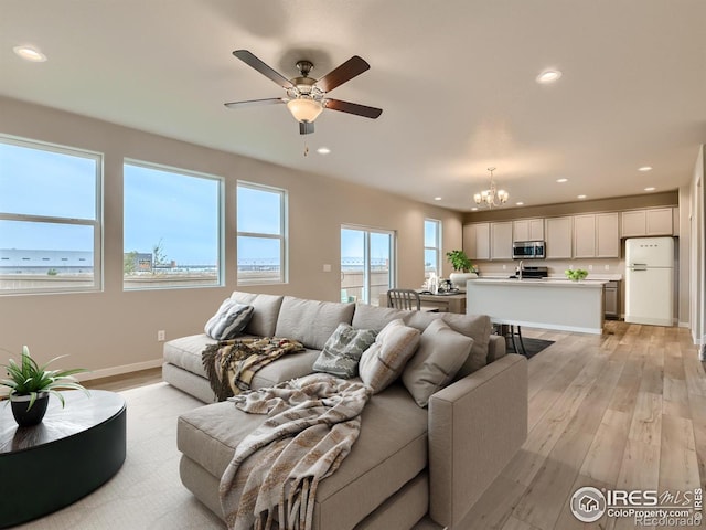 living room featuring ceiling fan with notable chandelier and light hardwood / wood-style flooring