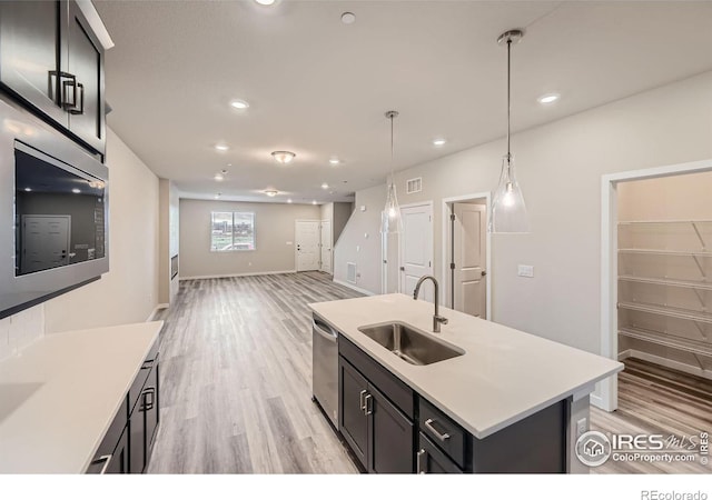 kitchen with decorative light fixtures, light hardwood / wood-style floors, a kitchen island with sink, appliances with stainless steel finishes, and sink