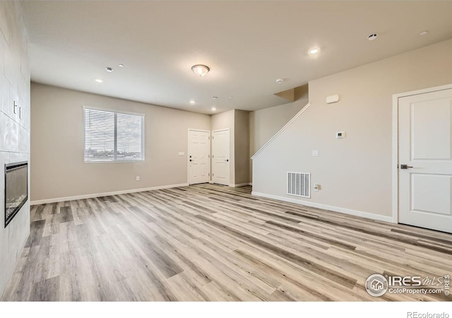 unfurnished living room with light wood-type flooring and a tiled fireplace