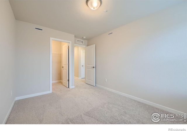 unfurnished bedroom featuring a walk in closet, a closet, and light carpet