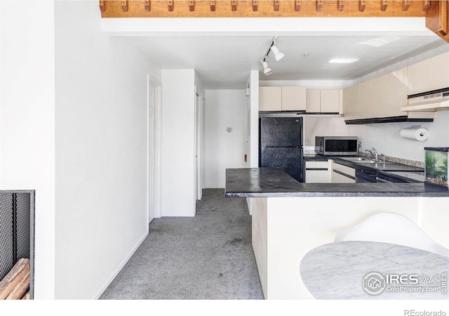 kitchen with cream cabinetry, black fridge, a kitchen breakfast bar, light carpet, and kitchen peninsula