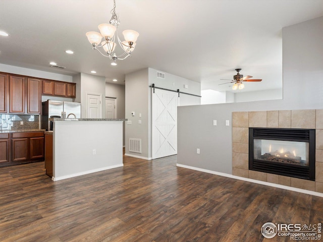 kitchen with ceiling fan with notable chandelier, a barn door, dark hardwood / wood-style floors, stainless steel refrigerator with ice dispenser, and pendant lighting