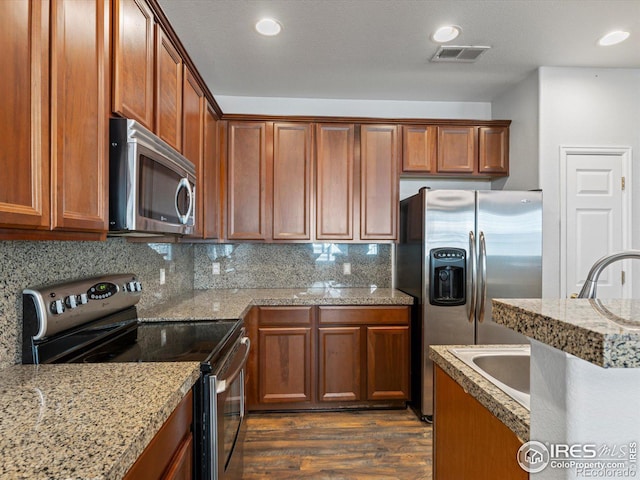 kitchen with appliances with stainless steel finishes, light stone countertops, dark hardwood / wood-style flooring, a textured ceiling, and backsplash