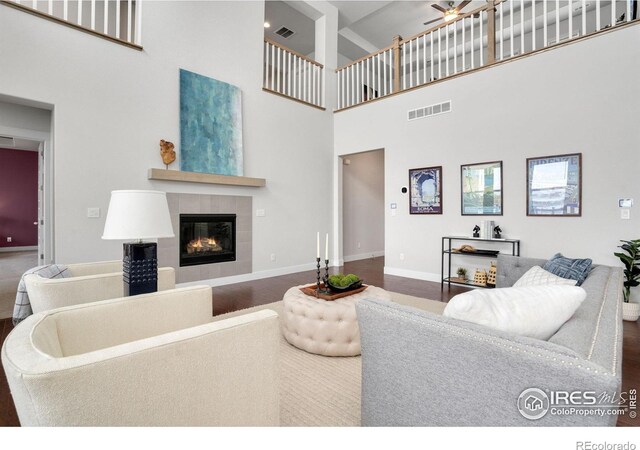 living room featuring a tiled fireplace, dark wood-type flooring, and a high ceiling