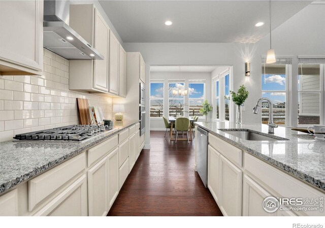 kitchen with sink, light stone counters, pendant lighting, wall chimney range hood, and stainless steel appliances