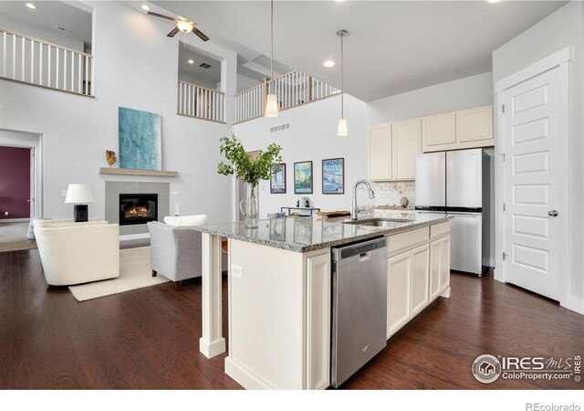 kitchen featuring appliances with stainless steel finishes, a center island with sink, light stone countertops, pendant lighting, and sink