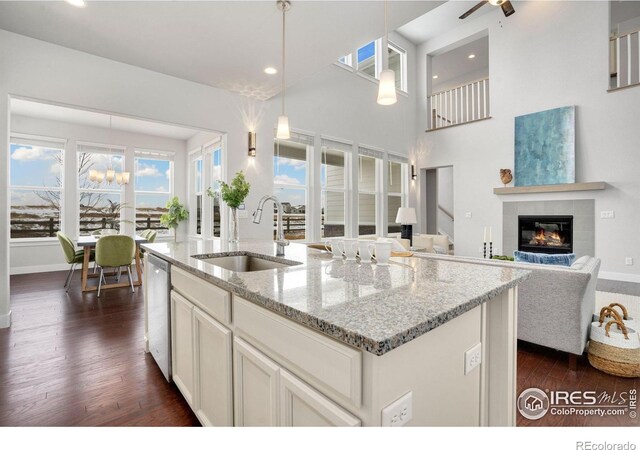 kitchen featuring sink, dishwasher, decorative light fixtures, light stone countertops, and a kitchen island with sink