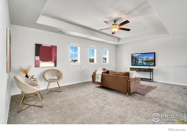 living room featuring a raised ceiling, ceiling fan, and carpet flooring