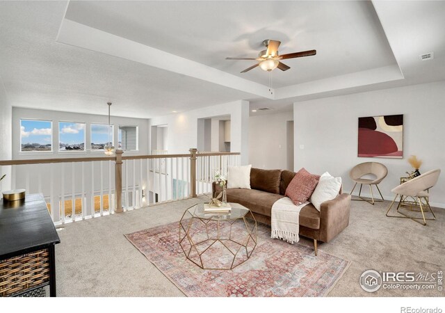 carpeted living room with ceiling fan and a tray ceiling