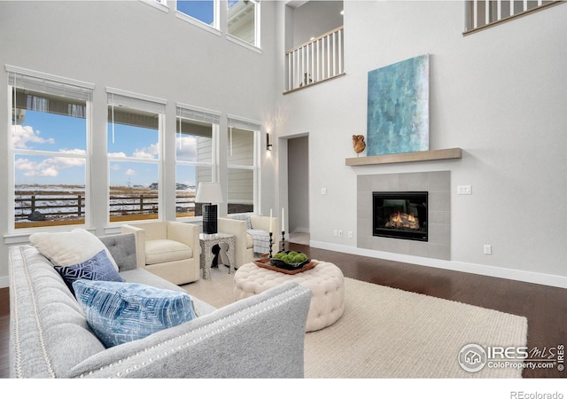 living room with a high ceiling, dark wood-type flooring, a tiled fireplace, and a healthy amount of sunlight